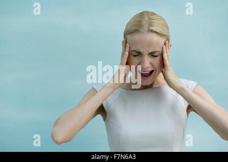 Woman holding head and screaming with eyes closed Stock Photo