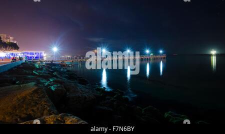 The Limassol pier in Enaerios Area in Cyprus. A night view of the city lights and the moon rising from the sea reflected in the Stock Photo