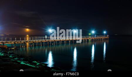 The Limassol pier in Enaerios Area in Cyprus. A night view of the city lights aligning to the moon as it rises from the sea refl Stock Photo