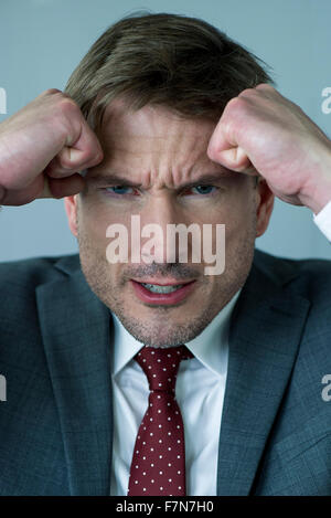 Businessman holding clenched fists against head in anger, portrait Stock Photo