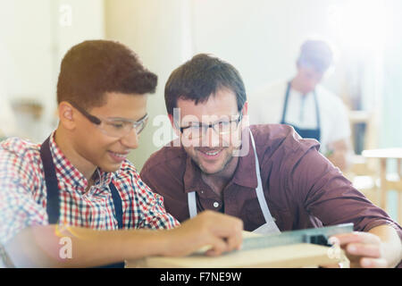 Smiling carpenters measuring wood with ruler in workshop Stock Photo