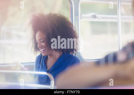 Smiling woman with afro texting with cell phone on bus Stock Photo