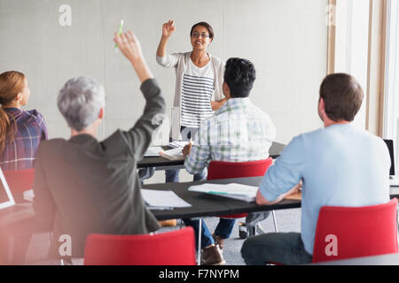 Teacher calling on student with hand raised in adult education classroom Stock Photo