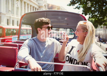 Enthusiastic girlfriend photographing boyfriend on double-decker bus Stock Photo