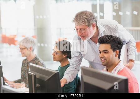 Professor helping student at computer in adult education classroom Stock Photo