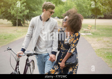 Couple walking with bicycle in park Stock Photo