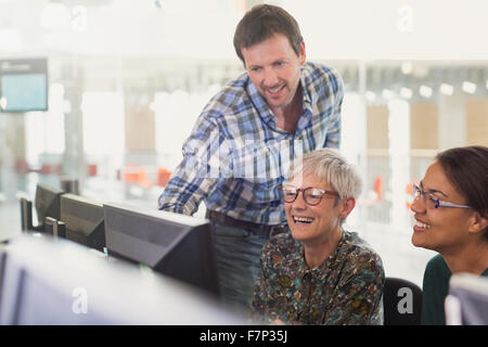 Smiling students at computer in adult education classroom Stock Photo