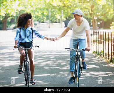Couple holding hands riding bicycles in urban park Stock Photo