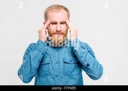 Young depressed handsome bearded man in jeans shirt touching his temples and having a headache over white background Stock Photo