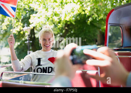 Woman waving British flag being photographed on double-decker bus Stock Photo