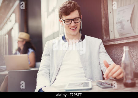 Smiling young man listening to music with headphones and mp3 player at sidewalk cafe