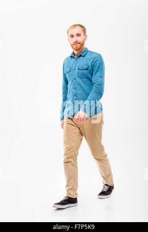 Positive attractive young male with beard walking and looking camera over white background Stock Photo
