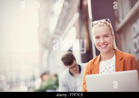 Portrait smiling blonde woman with laptop at sidewalk cafe Stock Photo