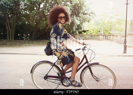 Portrait smiling woman with afro riding bicycle in urban park Stock Photo