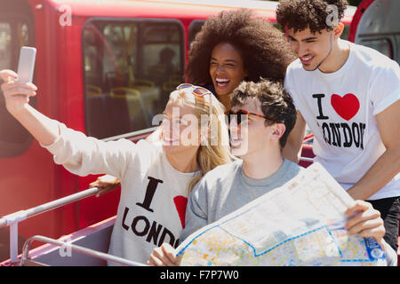 Friends with map taking selfie on double-decker bus Stock Photo