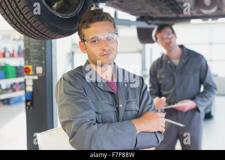 Portrait confident mechanic under car in auto repair shop Stock Photo