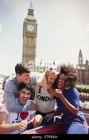 Enthusiastic friends riding double-decker bus below Big Ben clocktower, London, United Kingdom Stock Photo