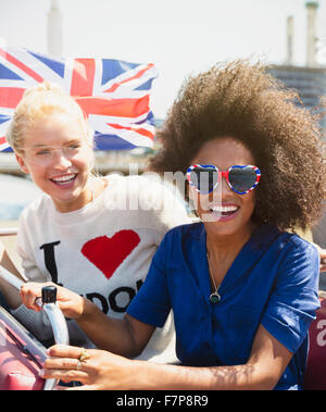 Portrait enthusiastic friends with British flag riding double-decker bus Stock Photo