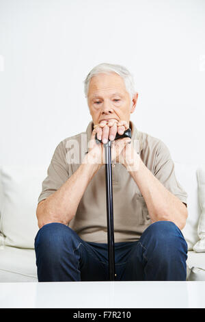 Sad old man with cane sitting pensive on a sofa Stock Photo