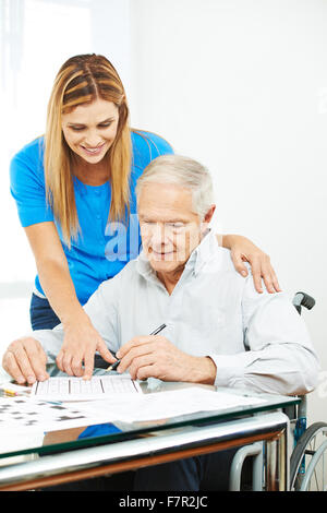 Daughter helping senior father in wheelchair at home solving sudoku puzzles Stock Photo