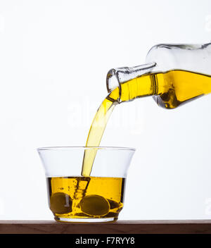 Extra virgin olive oil being poured from a bottle into a glass. Stock Photo