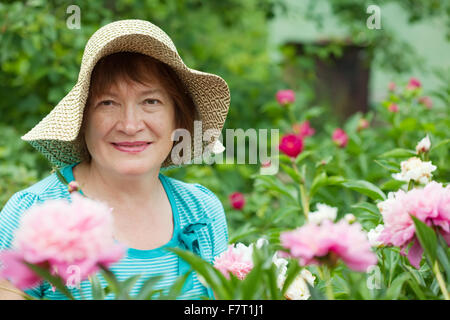 Happy mature woman in yard gardening with peony plant Stock Photo