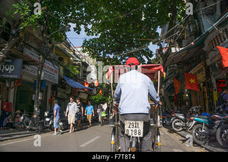 Hanoi, Vietnam: A cyclo driver rides past a typical street scene in Hanoi's vibrant Old Quarter. Stock Photo