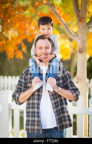 Happy Mixed Race Boy Riding Piggyback on Shoulders of Caucasian Father. Stock Photo