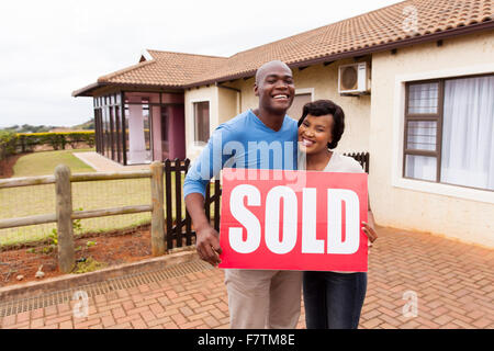 happy African couple standing outside their house and holding sold sign Stock Photo