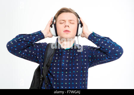 Concentrated serious young male in plaid shirt with backpack listening to music using headphones with eyes closed over white bac Stock Photo