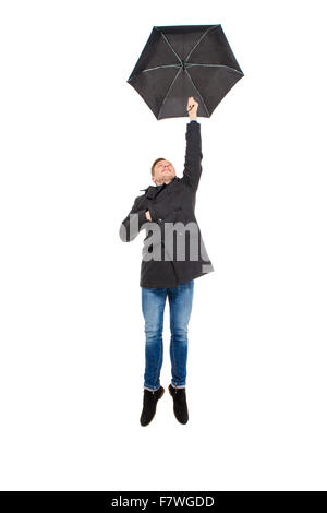 Attractive handsome young man in black coat and jeans flying with umbrella over white background Stock Photo