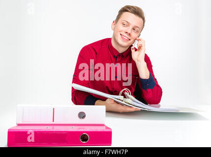 Playful cheerful attractive young man in red shirt using binders and talking on cellphone over white background Stock Photo