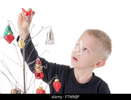 Cute little Boy decorates metal Christmas tree with beautiful glass Christmas ornaments, isolated on white Stock Photo