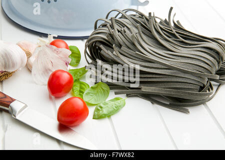 noodles, garlic, tomatoes and basil leaves on white table Stock Photo