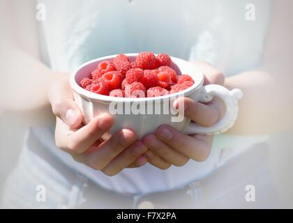 Close-up of girl holding raspberries in a cup