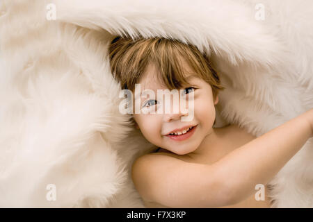 Portrait of a smiling boy wrapped in a fur rug Stock Photo