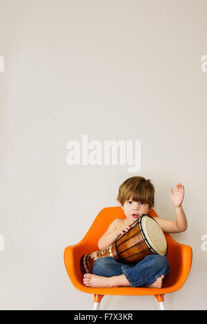 Boy sitting on a chair playing drum Stock Photo