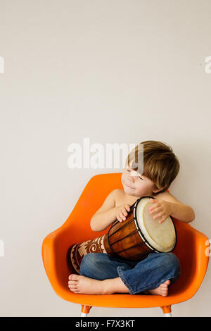Boy sitting on a chair playing drum Stock Photo