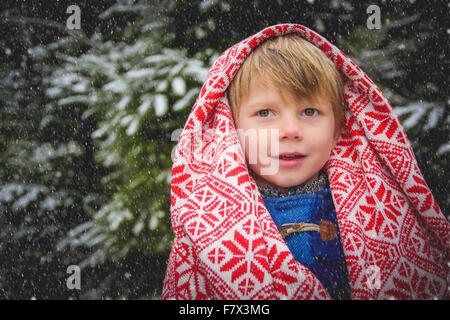 Portrait of smiling boy wrapped in a blanket in the snow Stock Photo