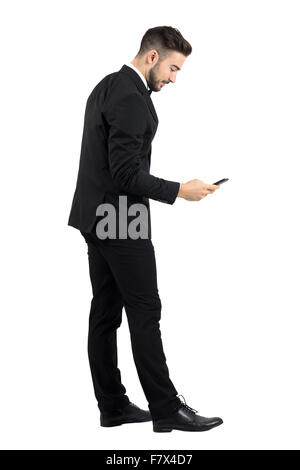 Side view of young businessman in suit typing message on smartphone touchscreen. Full body length portrait isolated over white Stock Photo