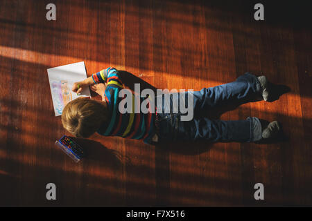 Overhead view of a boy lying on floor drawing a picture