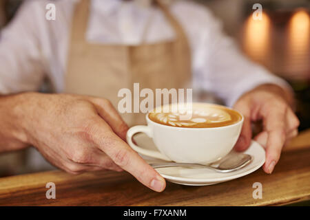 Close up of man serving coffee at cafe. Focus on male hands placing a cup of coffee on wooden counter. Stock Photo