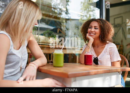 Image of young african girl sitting with her friend at outdoor cafe. Two young women meeting at sidewalk cafe having mocktails. Stock Photo