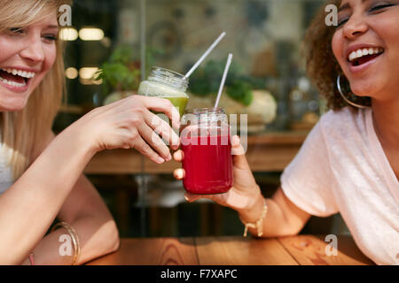 Close up shot of young friends toasting drinks at sidewalk cafe. Two happy women enjoying drinks and chat at outdoor coffee shop