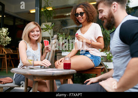 Group of friends playing a game of cards in a cafe. Woman picking up a playing card on table and smiling. Stock Photo