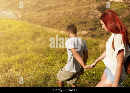 Outdoor shot of young couple enjoying on their vacation, walking down a peak holding hands. Caucasian couple hiking on a summer