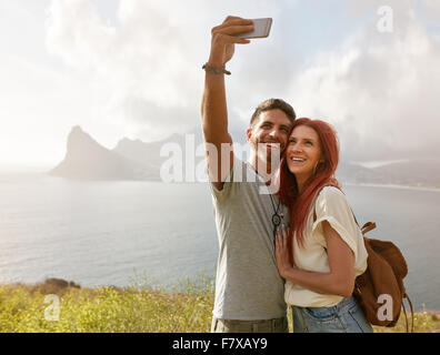 Cheerful young couple on holidays making selfie with smart phone. Young couple by the bay taking a selfie portrait with cell pho Stock Photo