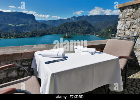 Served table with emty plate outdoor. View over lake Bled, island with church and Alps mountains in the background. Slovenia. Stock Photo