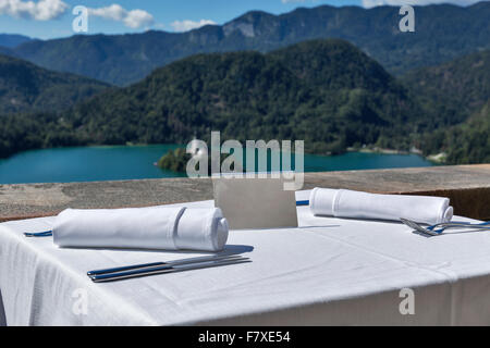Served table with empty plate outdoor. View over lake Bled, island with church and Alps mountains in the background. Slovenia. Stock Photo
