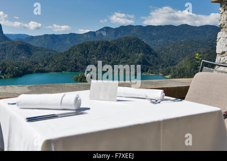 Served table with empty plate outdoor. View over lake Bled, island with church and Alps mountains in the background. Slovenia. F Stock Photo